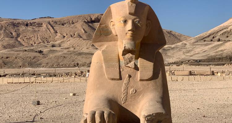 Stone statue of a Pharaoh in a desert landscape.