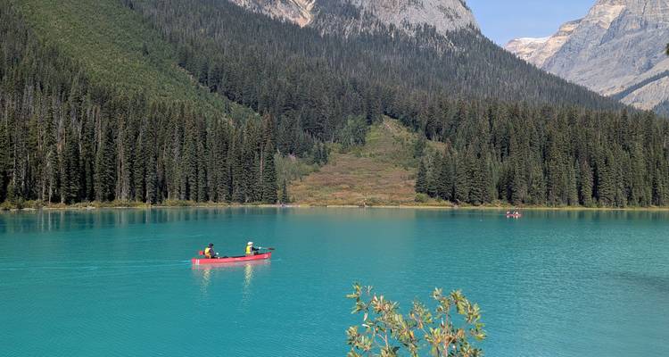 Canoe on a turquoise lake with forest and mountains in the background.