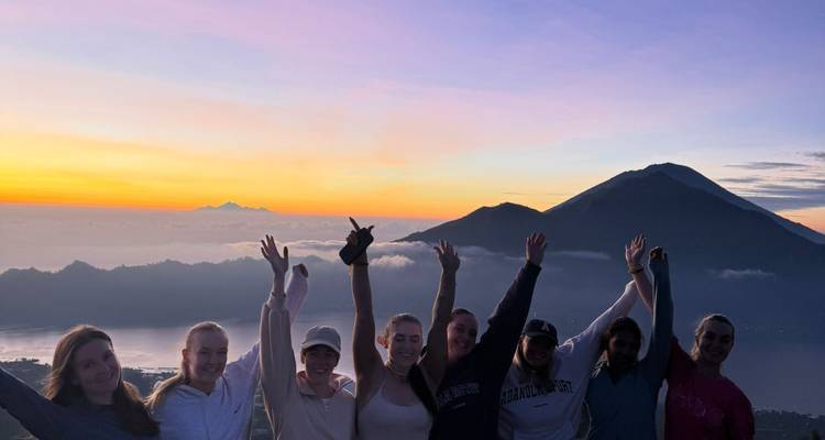 Group of people cheering at sunrise on a mountaintop.