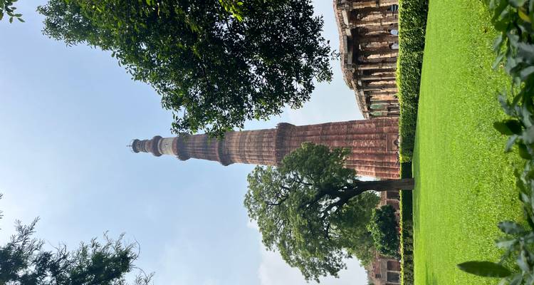 Qutb Minar con césped verde y árboles.