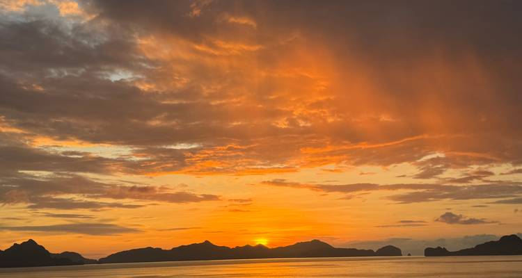 Kleurrijke zonsondergang boven een kalme zee met silhouetten van eilanden.