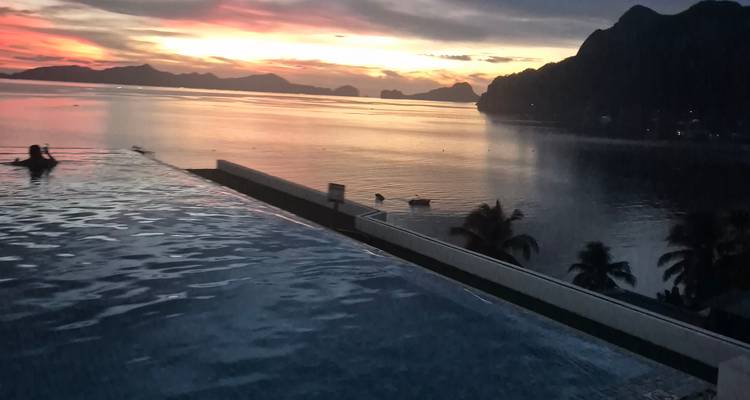 Piscina infinita con vista a un atardecer con océano y montañas.