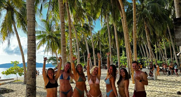 Groupe de personnes sur une plage tropicale entourée de palmiers.
