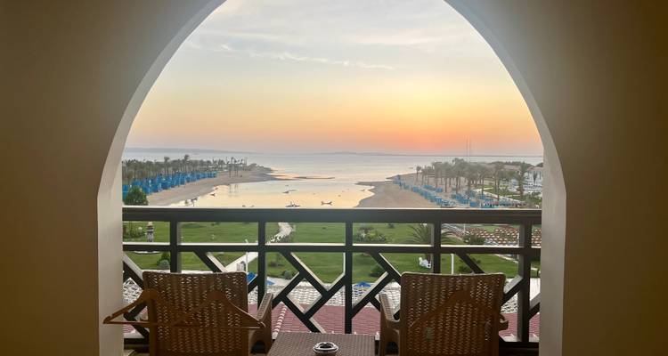 View of a balcony overlooking a beach at sunset.