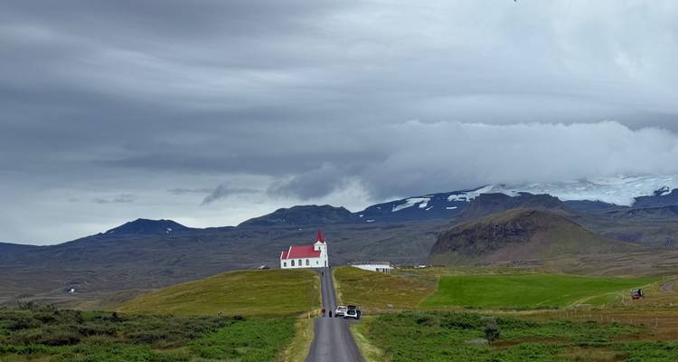 Vue pittoresque d'une église sur une colline avec des montagnes en arrière-plan.