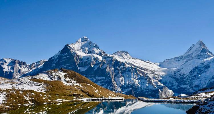 Snow-capped mountains reflecting in a clear lake under a blue sky.