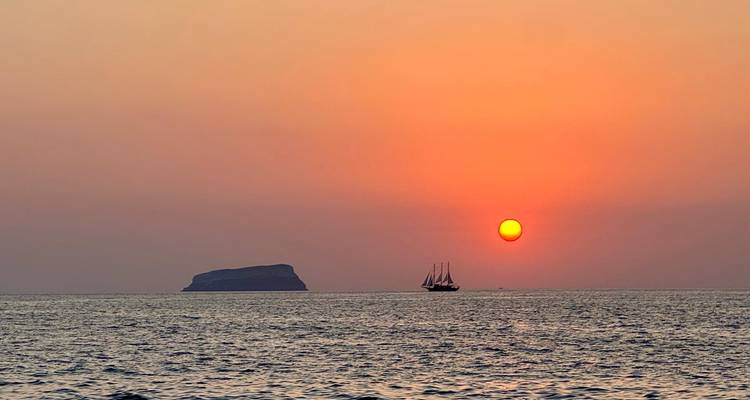 A majestic sunset over the sea with a distant sailboat.