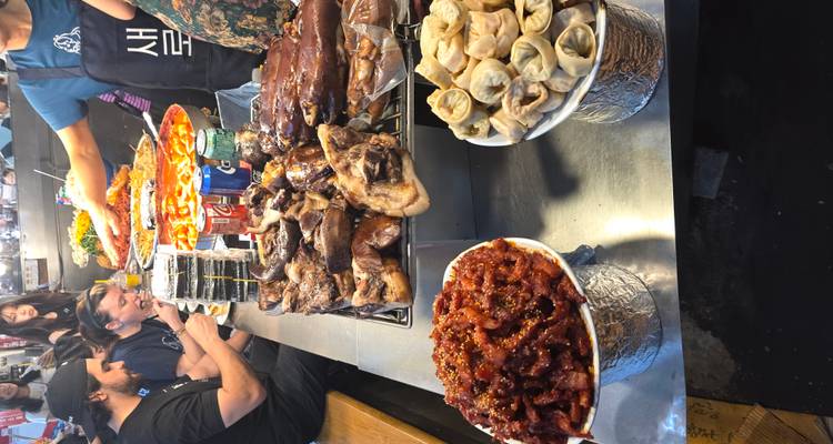 People enjoying street food at a market with various dishes displayed.