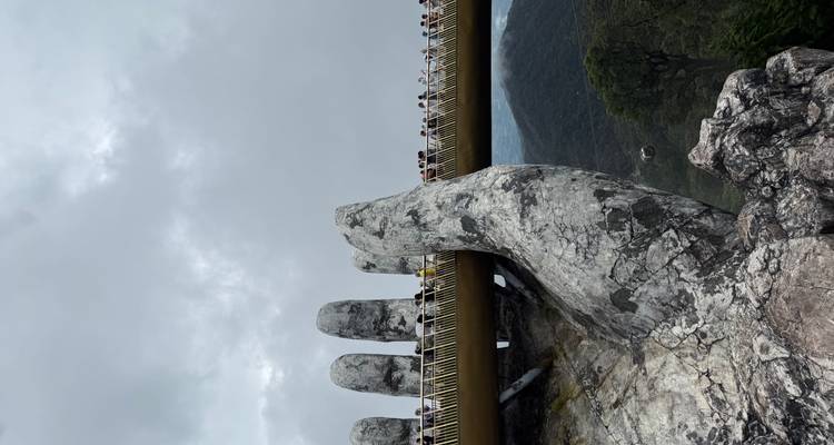 Golden Bridge with hand sculptures in foggy mountains.