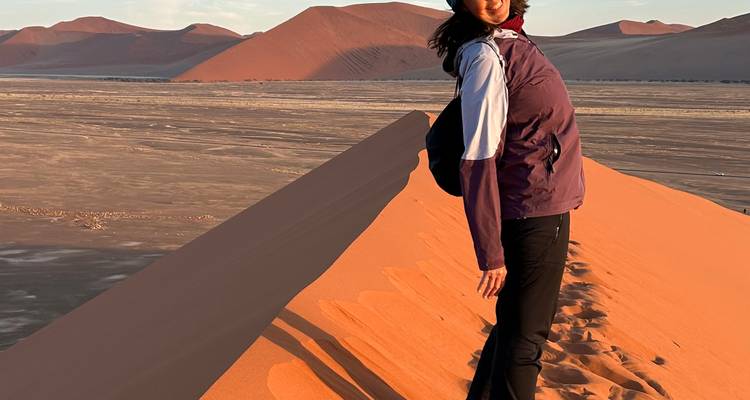 Une femme debout sur une dune de sable pendant le coucher du soleil.