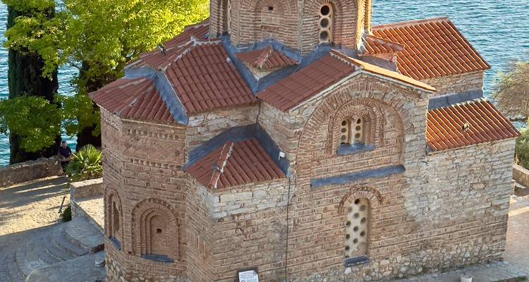 Small ancient church by the water with a red roof.