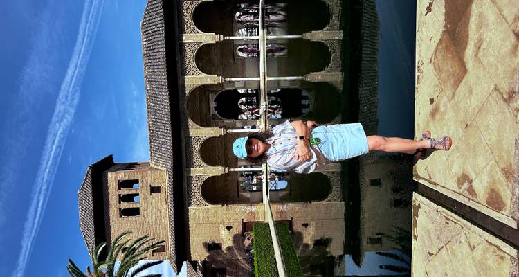 Femme debout près d'une piscine avec des arches réfléchissantes et une tour en arrière-plan.