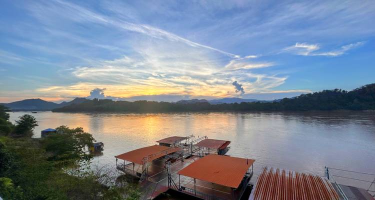 Sunset over a river with mountains and boats.