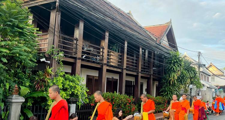 Monks in orange robes walking by a traditional wooden building.