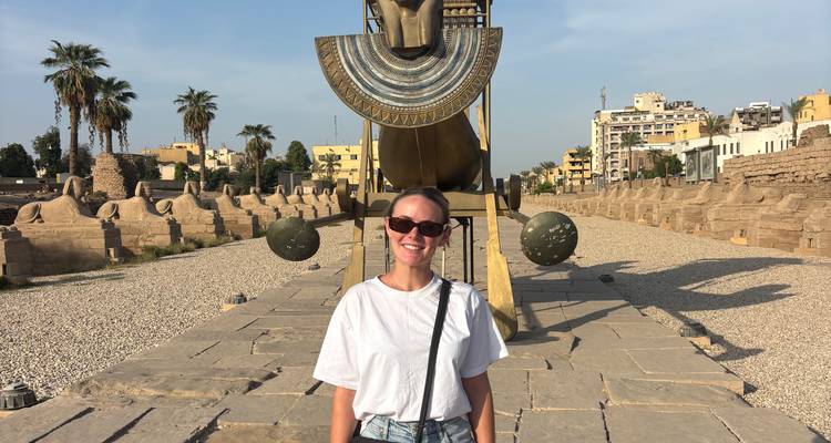 A tourist in front of the avenue of sphinxes with ancient structures.