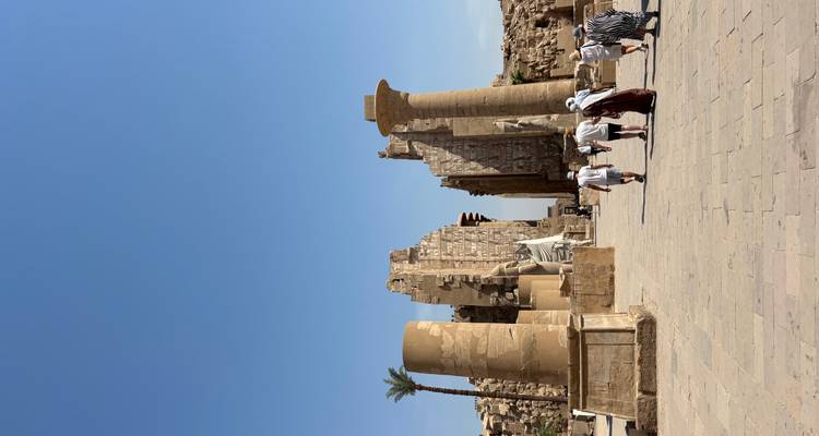 People walking in ancient ruins with large columns and stone structures.