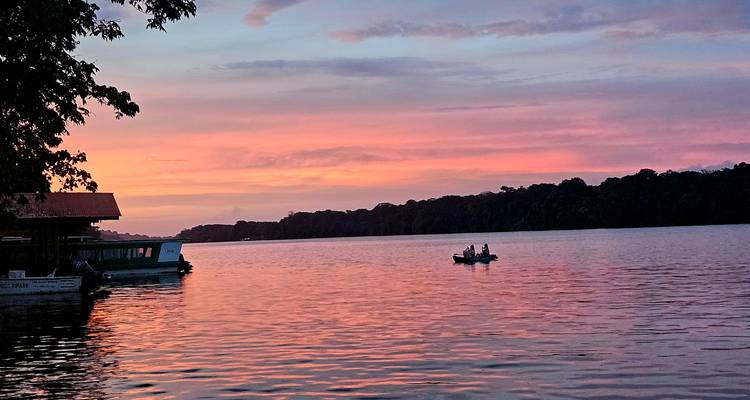 Coucher de soleil sur une rivière avec un petit bateau et silhouette d'arbres.