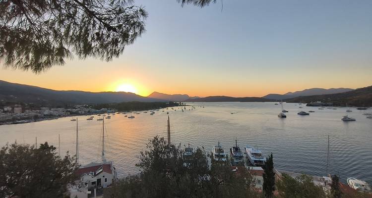 Coucher de soleil sur une baie avec des voiliers et des montagnes.