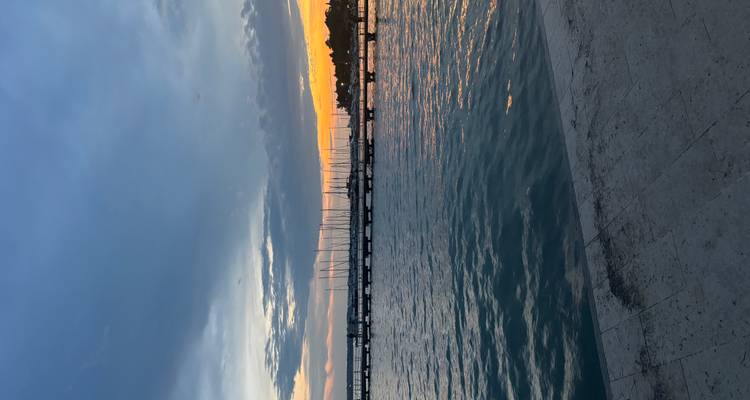 Sunset view over a pier with sailboats on the water.