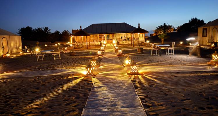 Camp du désert éclairé avec un sentier bordé de lanternes la nuit.