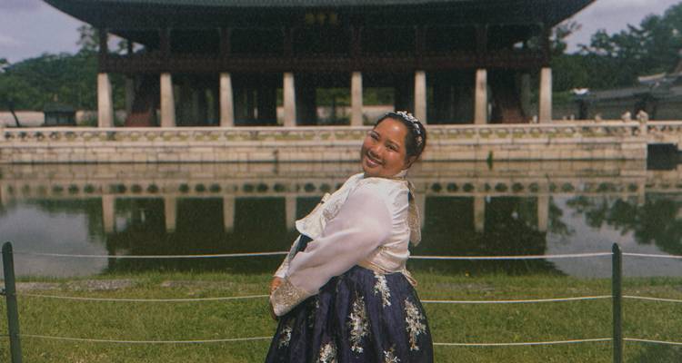 Person in traditional hanbok posing by a pond.