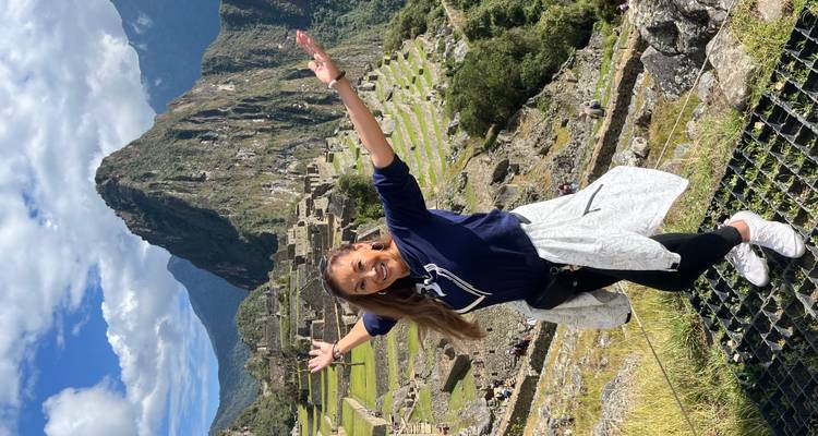 Woman celebrating with open arms at Machu Picchu against a backdrop of the ancient ruins.