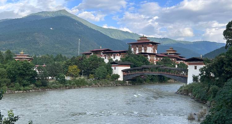 A picturesque Bhutanese fortress with a river flowing in front, surrounded by mountains.