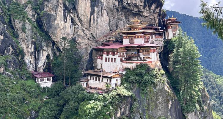 A monastery perched on a cliffside amidst lush green forests and mountains.
