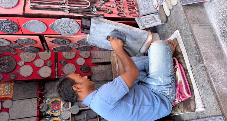 A man working on a stone carving in a shop filled with various plaques and decorations.