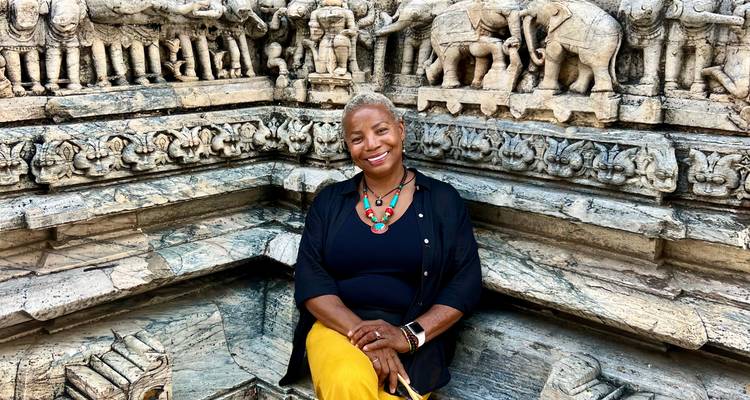 Een persoon die zit voor een ingewikkeld gesneden stenen muur met olifantmotieven.