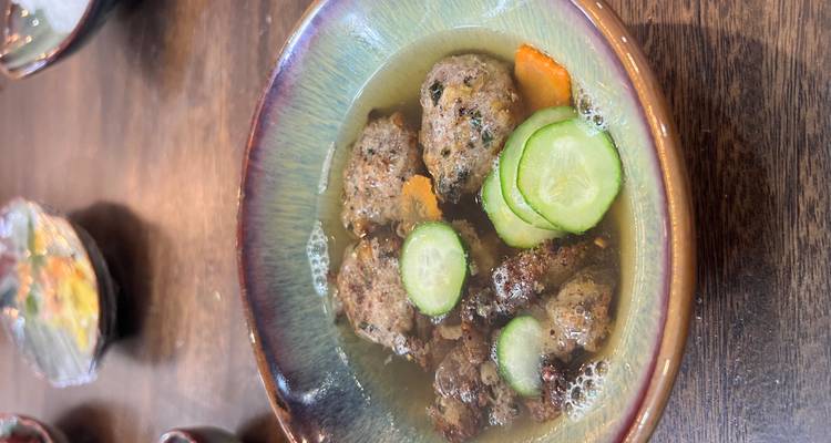 A bowl of soup with meatballs and slices of cucumber, part of a meal preparation.