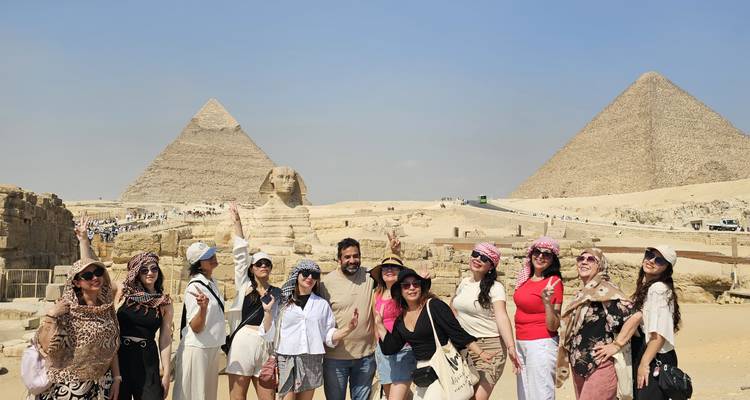 Groupe de personnes souriantes et posant devant des pyramides et un sphinx.