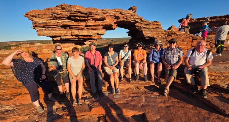 A group of tourists posing on rocky terrain with an arch formation in the background.