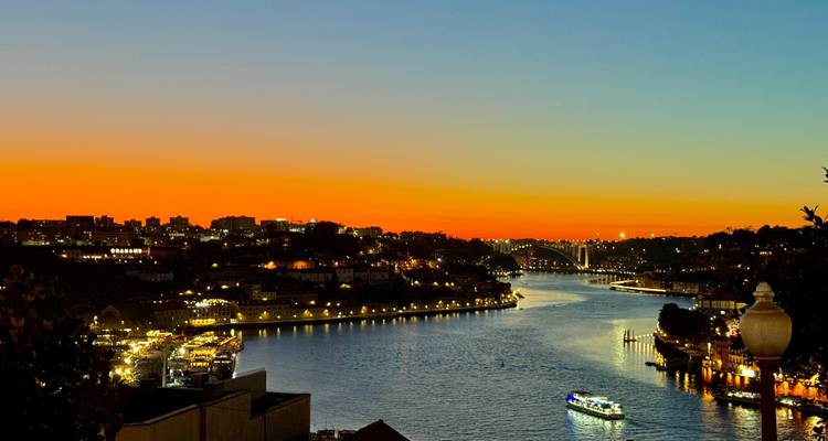 Ein lebendiger Sonnenuntergang über einem Fluss mit Stadtlichtern und Booten.