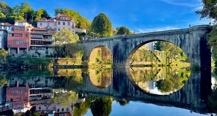 Eine Steinbrücke über einem ruhigen Fluss mit Spiegelungen.