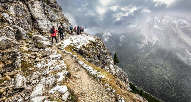Randonneurs marchant le long d'un sentier de montagne étroit avec de la neige.