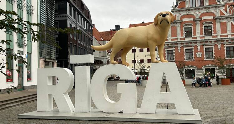 Gran letrero de RIGA con estatua de perro y edificios históricos.