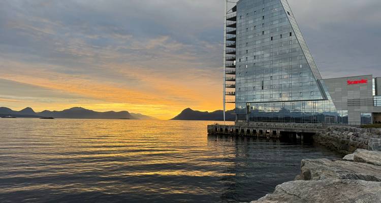 Un bâtiment moderne en verre surplombant un plan d'eau au coucher du soleil.