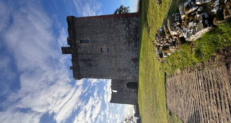Ruines d'un château en pierre sur une colline herbeuse sous un ciel bleu.