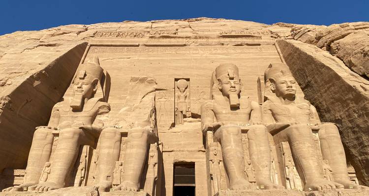 Des statues colossales de pharaons sculptées dans une façade rocheuse.