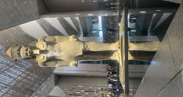 Large statue of an ancient Egyptian figure inside a modern building with reflective floors.