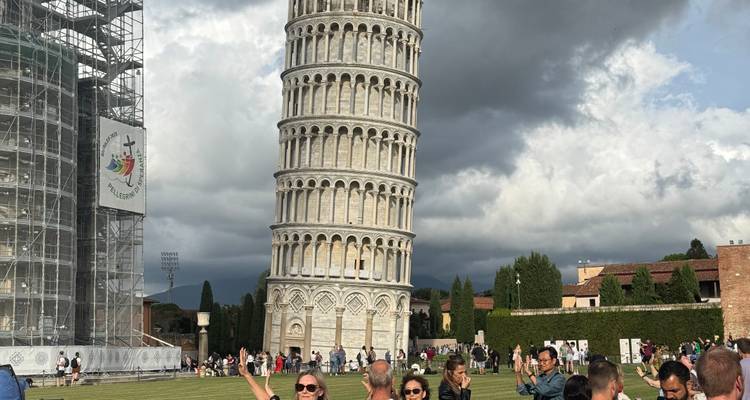 Visitors posing near the Leaning Tower of Pisa on a cloudy day.
