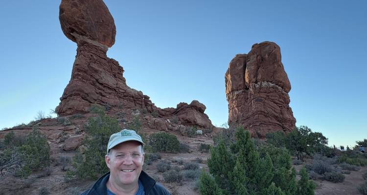 Man poseert voor balancerende rotsformaties.