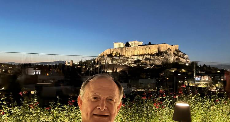 Person posing with the Acropolis lit up at night.