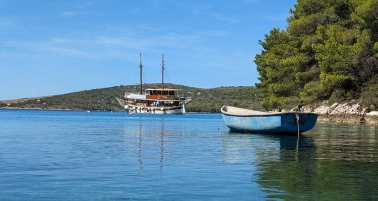 Petit bateau flottant sur une eau calme avec un navire plus grand en arrière-plan.