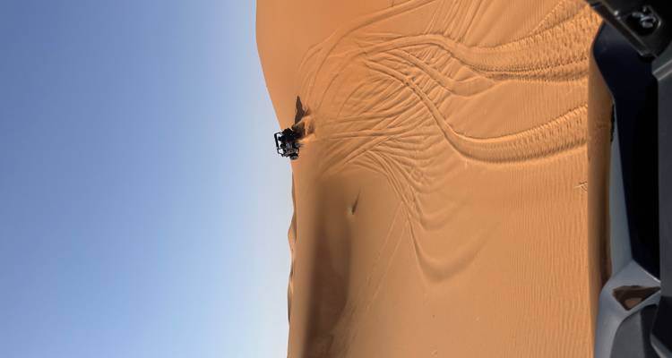 A vehicle ascending a sand dune in a desert landscape.