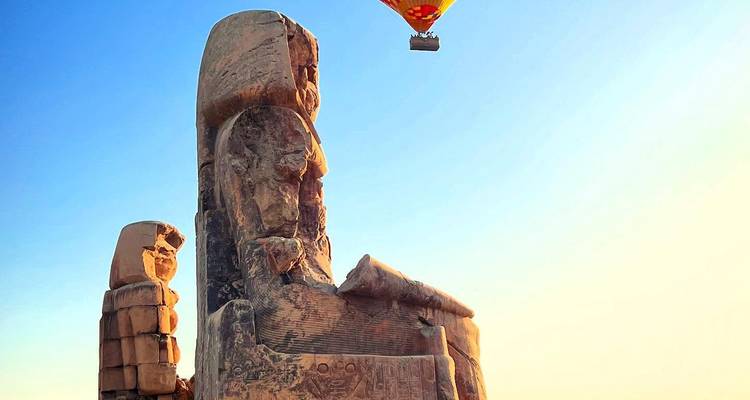 Hot air balloon floating over ancient stone statue.
