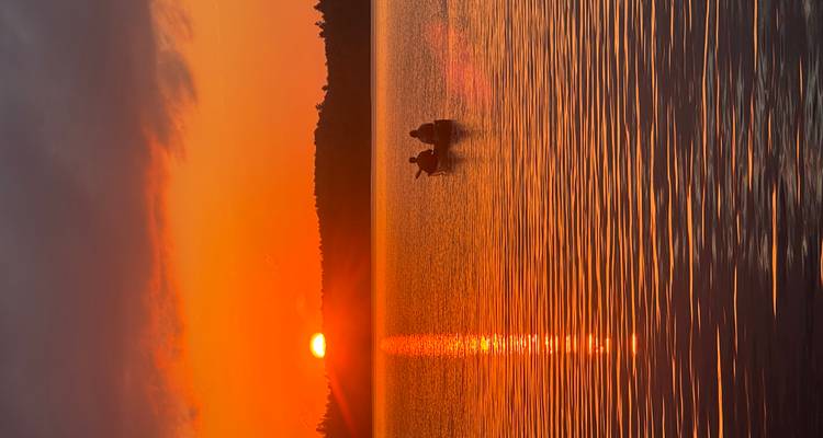 Canoë sur un lac au coucher du soleil avec un ciel vibrant.