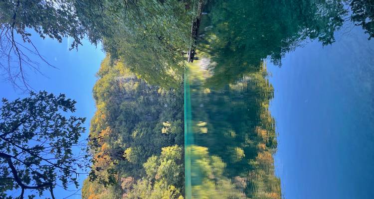 Lac avec une eau cristalline reflétant les arbres et le ciel bleu.