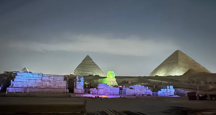 Une vue nocturne des pyramides et du Sphinx illuminés de lumières colorées.